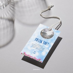 May include: A rectangular gift tag with a disco ball illustration and the words "THANK YOU!" in blue. The tag has a blue sky background with white bokeh and pink flowers at the bottom. A white string is attached.