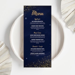 Puede incluir: Una tarjeta de menú azul marino con texto y detalles dorados, que presenta una lista de aperitivos, platos principales y postres. El menú está sobre un plato blanco, con un fondo azul oscuro y brillo dorado.