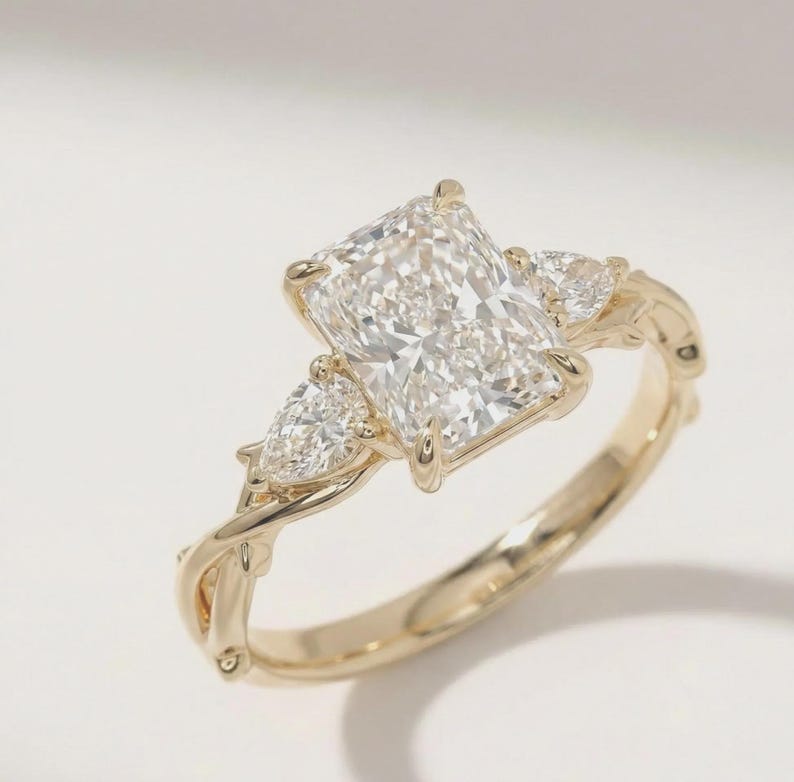 Radiant pear diamond three-stone ring from ExcellentJewels, crafted in custom gold for an elegant and timeless look. The central pear-cut diamond is accentuated by two side stones, creating a sophisticated engagement ring perfect for celebrating love, milestones, or special occasions with luxurious fine jewelry style.