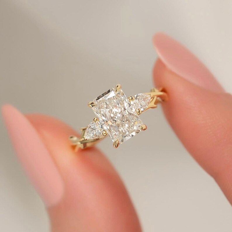 Three-stone pear diamond ring by ExcellentJewels, radiant cut for exceptional sparkle. Handcrafted engagement or statement ring with customizable options. Elegant, timeless design suitable for weddings, anniversaries, or personal collection. Perfect gift for couples or jewelry enthusiasts seeking meaningful and sophisticated fine jewelry. Radiant solitaire engagement ring with leaf design shank and pear diamonds.