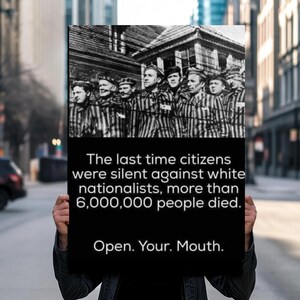 May include: A black and white poster held by a person in front of a blurred city background. The poster features a historical image of people in striped uniforms and text that reads: "The last time citizens were silent against white nationalists, more than 6,000,000 people died. Open. Your. Mouth."
