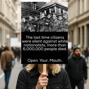 May include: A black and white sign held by a person in a crowd. The sign has a black background with white text that reads: "The last time citizens were silent against white nationalists, more than 6,000,000 people died. Open. Your. Mouth."