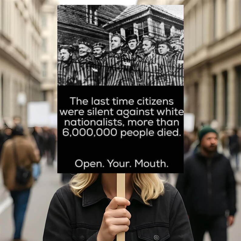 May include: A black and white sign held by a person in a crowd. The sign has a black background with white text that reads: "The last time citizens were silent against white nationalists, more than 6,000,000 people died. Open. Your. Mouth."