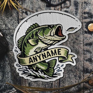 May include: Embroidered patch featuring a green and black bass fish leaping out of water. The fish is set against a white background with a fishing line and the word "ANYNAME" on a banner. The patch is on a denim background.