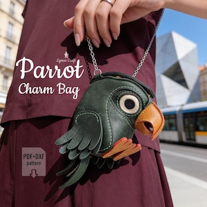 May include: A dark green parrot-shaped charm bag with a yellow-orange beak and feet, featuring a silver chain strap. The bag displays the text "Parrot Charm Bag" and "Lymar Craft" along with a "PDF+DXF pattern" icon with a downward arrow.