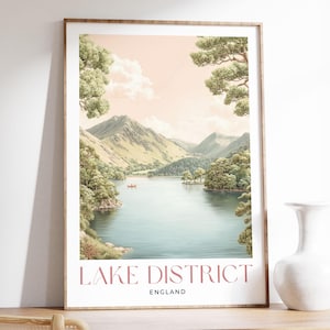 Può includere: Stampa incorniciata del Lake District in Inghilterra. L'opera raffigura un lago sereno circondato da alberi verdi e montagne sotto un cielo rosa tenue. Le parole "Lake District England" sono stampate in basso.