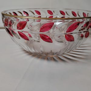 May include: A clear glass bowl featuring a gold-toned rim and a repeating pattern of embossed, vibrant red leaves encircling the upper exterior. The base of the bowl displays a subtle, radiating fluted design that catches the light.