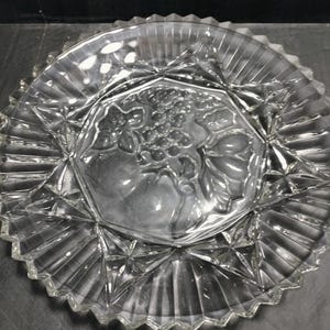 May include: A clear glass serving dish with a scalloped edge and a raised, embossed design of grapes in the center.