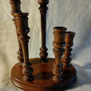 May include: A dark brown wooden candle holder with five individual candle holders. The candle holder has a round base and a central column, with four additional candle holders arranged around the center. The wood has a polished finish.