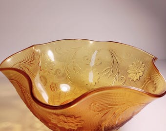 Pode incluir: Uma tigela vintage de vidro âmbar com uma borda ondulada e um padrão floral. A tigela é feita de vidro transparente com uma superfície texturizada.