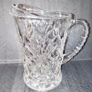 May include: A clear glass pitcher with a diamond pattern. The pitcher has a handle and a wide mouth.