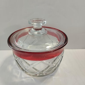 May include: A clear glass jar with a red band around the top and a matching lid. The jar has a diamond pattern.