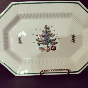 May include: White rectangular serving platter with a green border and a Christmas tree design in the center. The tree is decorated with ornaments and surrounded by gifts. The platter has a ribbed texture.
