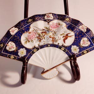 May include: A white porcelain fan-shaped dish with a blue and gold floral design. The dish features a gold rim and a white interior with a fan-like design.