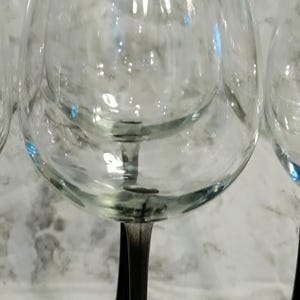 May include: Set of four clear glass wine glasses with black stems and bases. The glasses are round and have a wide bowl.