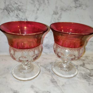 May include: Two clear glass goblets with a red iridescent top. The goblets have a clear glass stem and base.