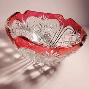 May include: A clear glass bowl with a red rim and intricate cut glass design. The bowl has a scalloped edge and is perfect for serving snacks or desserts.