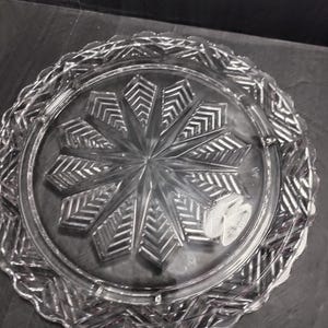 May include: A clear glass serving plate with a decorative starburst pattern and a scalloped edge.