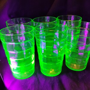May include: Six vintage, neon green drinking glasses. The glasses have a grid-like pattern and a rounded base. The glasses are arranged on a dark purple surface. The glasses are made of a transparent material.