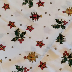 May include: A white fabric featuring a repeating pattern of green holly leaves with red berries, red and yellow plaid stars, and stylized Christmas trees in red, yellow, and green plaid. Small gold-colored stars are scattered across the background.
