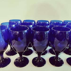 May include: A collection of cobalt blue wine glasses. The glasses have a dark blue stem and base, with a rounded bowl. The glasses are arranged in rows, with the stems and bases visible. The glasses are made of glass.