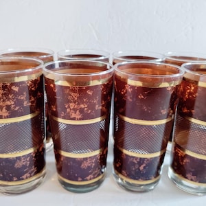 May include: Set of eight vintage highball glasses. Each glass features a dark burgundy background with gold accents and a gold rim. The design includes a gold band and a black mesh pattern.