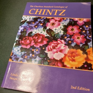 May include: A book titled "The Charlton Standard Catalogue of CHINTZ" with a floral cover design. The cover features pink, red, and yellow roses, with blue and white flowers. The book is a 2nd Edition.