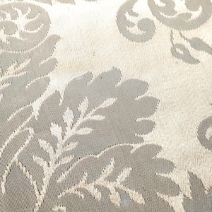 May include: Close-up of a beige fabric with a subtle, embossed floral pattern. The fabric has a textured, woven look and features a repeating design of stylized leaves and flowers.
