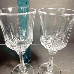 May include: Two clear glass wine glasses with a cut crystal design. The glasses have a tall, slender stem and a round base.