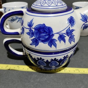 May include: A blue and white porcelain teapot with a floral design. The teapot has a lid and a handle. The teapot is sitting on a table.