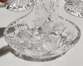 May include: A clear, cut-glass basket with a handle, showcasing intricate starburst and diamond patterns. The basket is designed with a rounded bowl and a sturdy, arched handle, perfect for decorative use or serving.