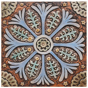 Könnte beinhalten: Eine Keramikfliese mit einem blauen, grünen und goldenen floralen Design. Die Fliese hat eine erhabene, strukturierte Oberfläche und ist vor einem braunen Hintergrund platziert.