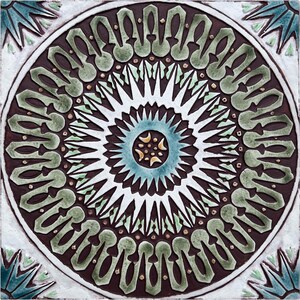 Op de afbeelding: Een keramische tegel met een geometrisch ontwerp in bruin, wit, groen en blauw. Het ontwerp heeft een centrale stervorm met concentrische cirkels van herhalende patronen.