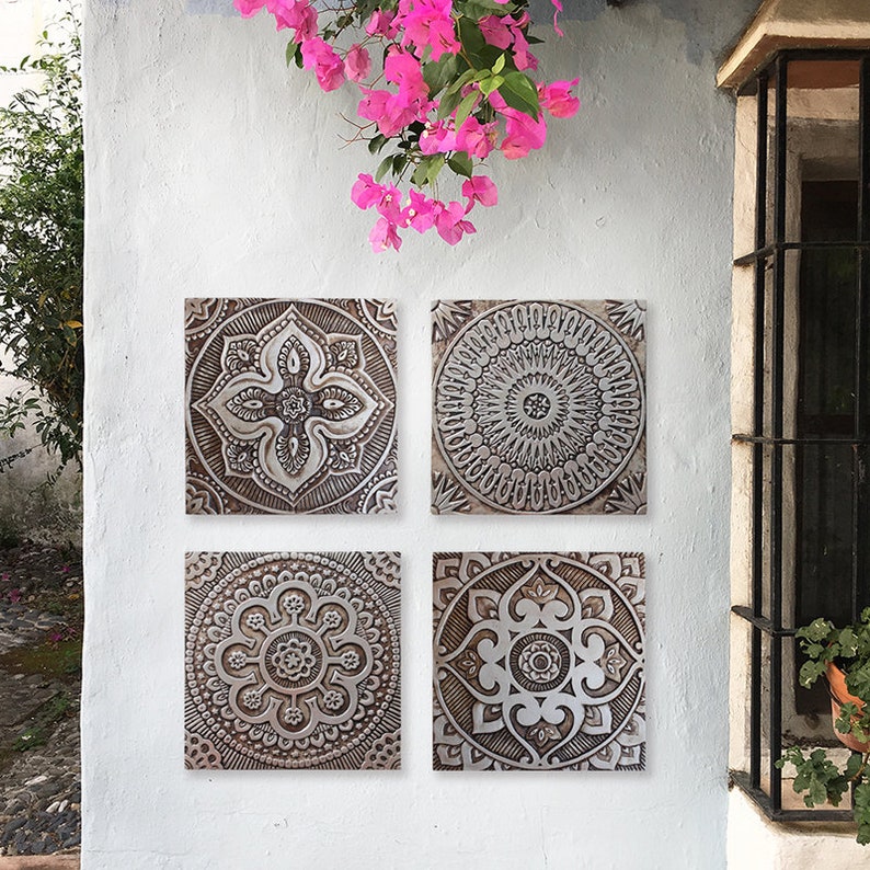 May include: Set of four square wall decor tiles with intricate embossed designs in shades of brown and white. The tiles feature a variety of geometric patterns, including a mandala, a floral design, and a starburst.