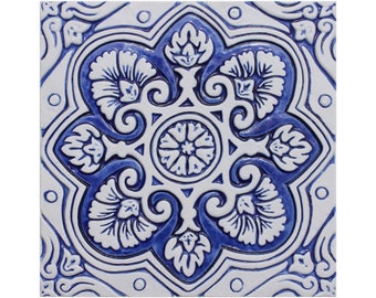 May include: A blue and white ceramic tile with a floral design. The tile has a central motif of a flower with eight petals, surrounded by four smaller flowers. The tile is decorated with intricate swirls and lines.