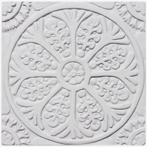 Op de afbeelding: Witte keramische tegel met een reliëf, gegraveerd ontwerp van een cirkelvormig bloemenpatroon. De tegel heeft een getextureerd oppervlak en een witte achtergrond.