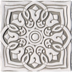 Op de afbeelding: Een witte keramische tegel met een grijs reliëfpatroon. Het patroon heeft een centrale cirkel omgeven door ingewikkelde bloemmotieven.