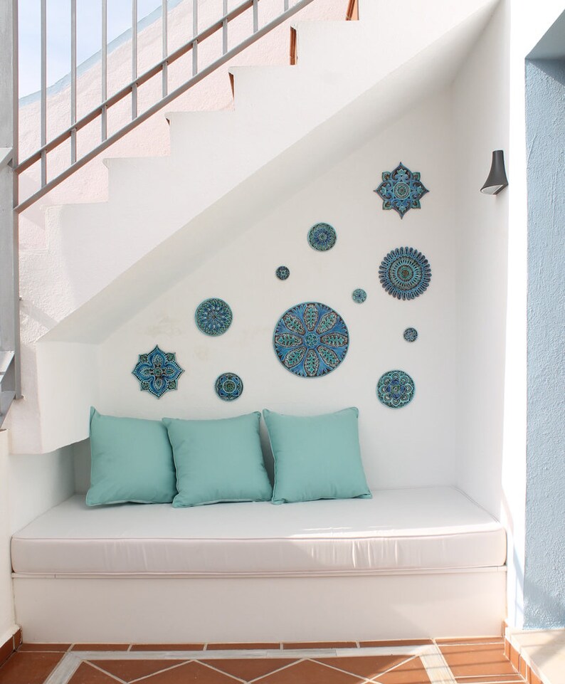 May include: A white bench with blue and green patterned cushions sits under a white staircase decorated with blue and green ceramic tiles.