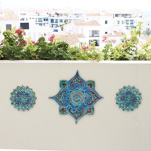 May include: Five blue and green ceramic wall tiles with intricate mandala designs. The tiles are arranged in a row on a white wall.