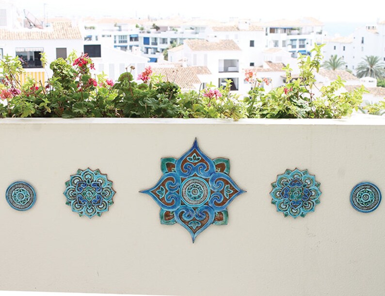 May include: Five blue and green ceramic wall tiles with intricate mandala designs. The tiles are arranged in a row on a white wall.