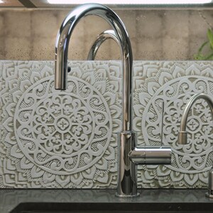 May include: A chrome kitchen faucet with a single lever handle and a spout that extends out and down. The faucet is mounted on a countertop with a decorative tile backsplash featuring a white mandala design.
