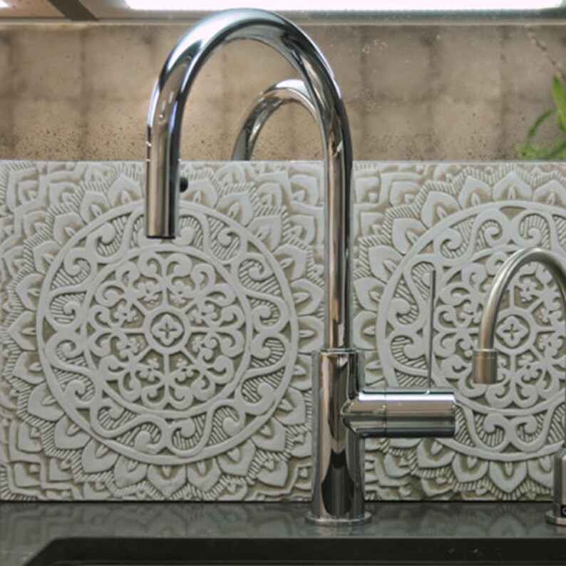 May include: A chrome kitchen faucet with a single lever handle and a spout that extends out and down. The faucet is mounted on a countertop with a decorative tile backsplash featuring a white mandala design.