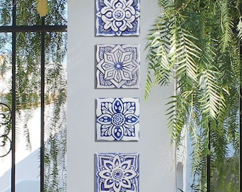 May include: Four blue and white ceramic tiles with intricate floral patterns. The tiles are arranged vertically on a white wall.