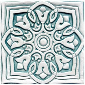 Op de afbeelding: Een witte keramische tegel met een ingewikkeld blauw en wit bloemmotief. De tegel heeft een reliëfpatroon.