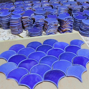 May include: A close-up of a blue mosaic tile pattern made of individual ceramic tiles shaped like fish scales. The tiles are arranged in a repeating pattern, creating a visually appealing design.