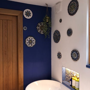 May include: A white bathtub with a blue and white tiled alcove above it. The alcove has two bottles of bath products. The wall behind the tub is painted a deep blue and decorated with several blue and white patterned ceramic plates.