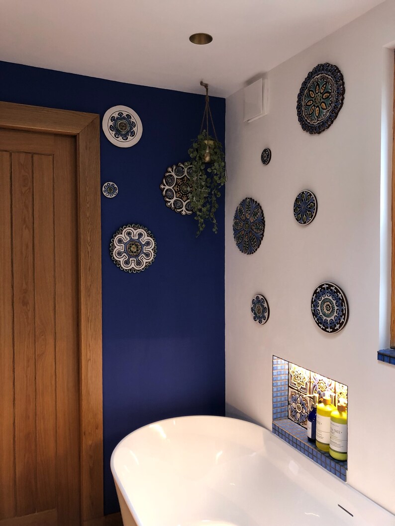 May include: A white bathtub with a blue and white tiled alcove above it. The alcove has two bottles of bath products. The wall behind the tub is painted a deep blue and decorated with several blue and white patterned ceramic plates.