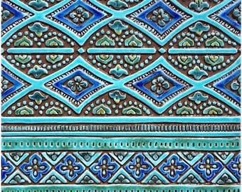 May include: A blue and brown ceramic tile with a geometric pattern. The tile has a repeating design of diamonds and squares with intricate details.