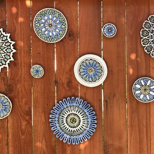 May include: A wooden wall with eight decorative ceramic plates with intricate geometric patterns in shades of blue, green, and yellow.