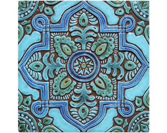 Pode incluir: Um azulejo de cerâmica quadrado com um padrão geométrico azul e verde. O azulejo tem um design em relevo e um fundo castanho.